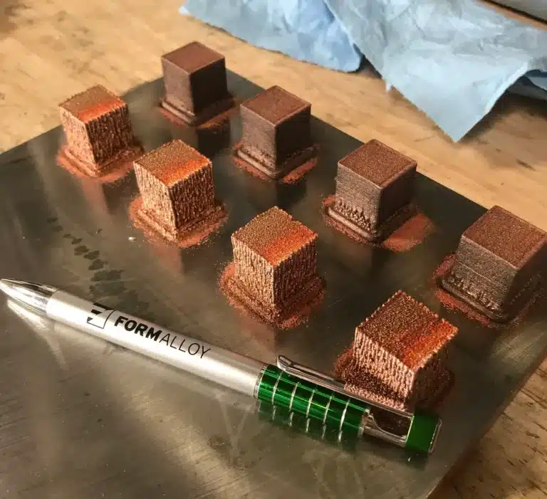 Pure Copper Deposition. Copper and Inconel 625 test cubes printed via infrared laser DED on metal substrate, shown with Form Alloy pen for scale.