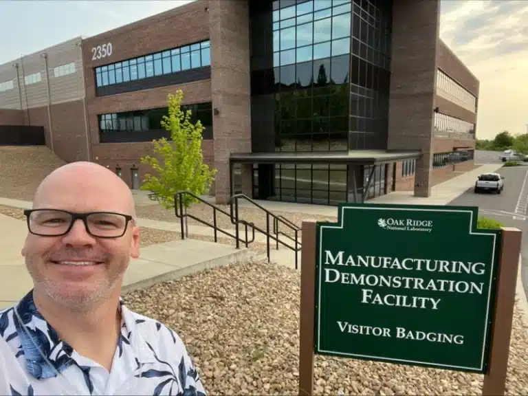Visitor at Oak Ridge National Laboratory's Manufacturing Demonstration Facility, located at 2350, posing in front of the building and visitor badging sign.