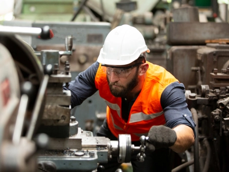 Factory worker operating industrial machinery while wearing safety gear.